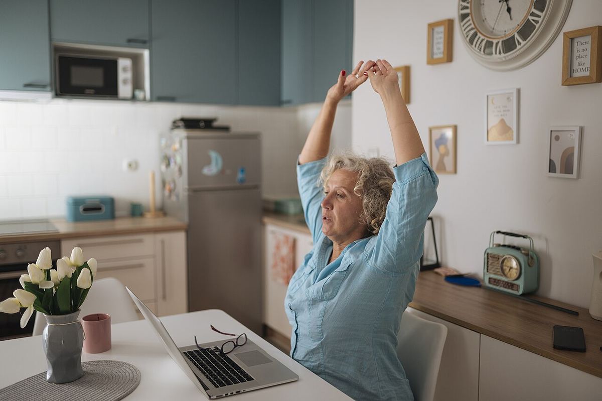 Vrouw rekt zich uit aan een bureau met laptop in een lichte keuken