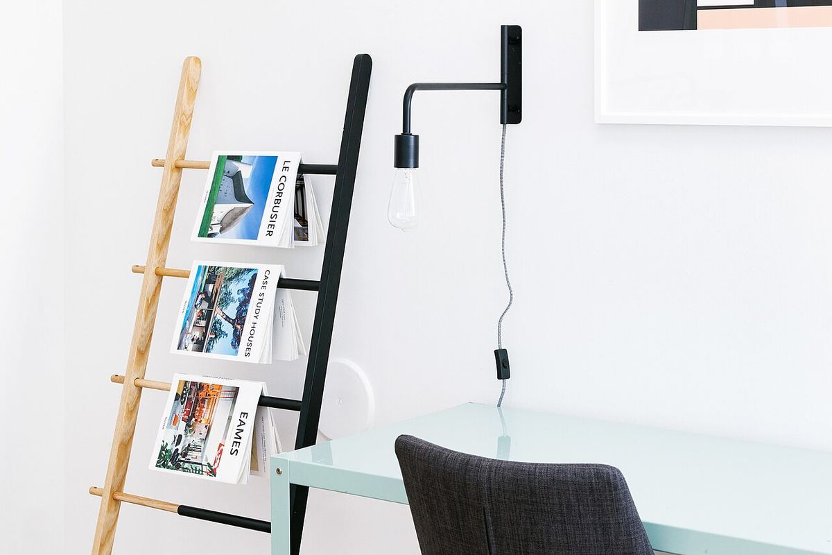 Witte kamer met een ladderrek, een wandlamp en een eenvoudig bureau
