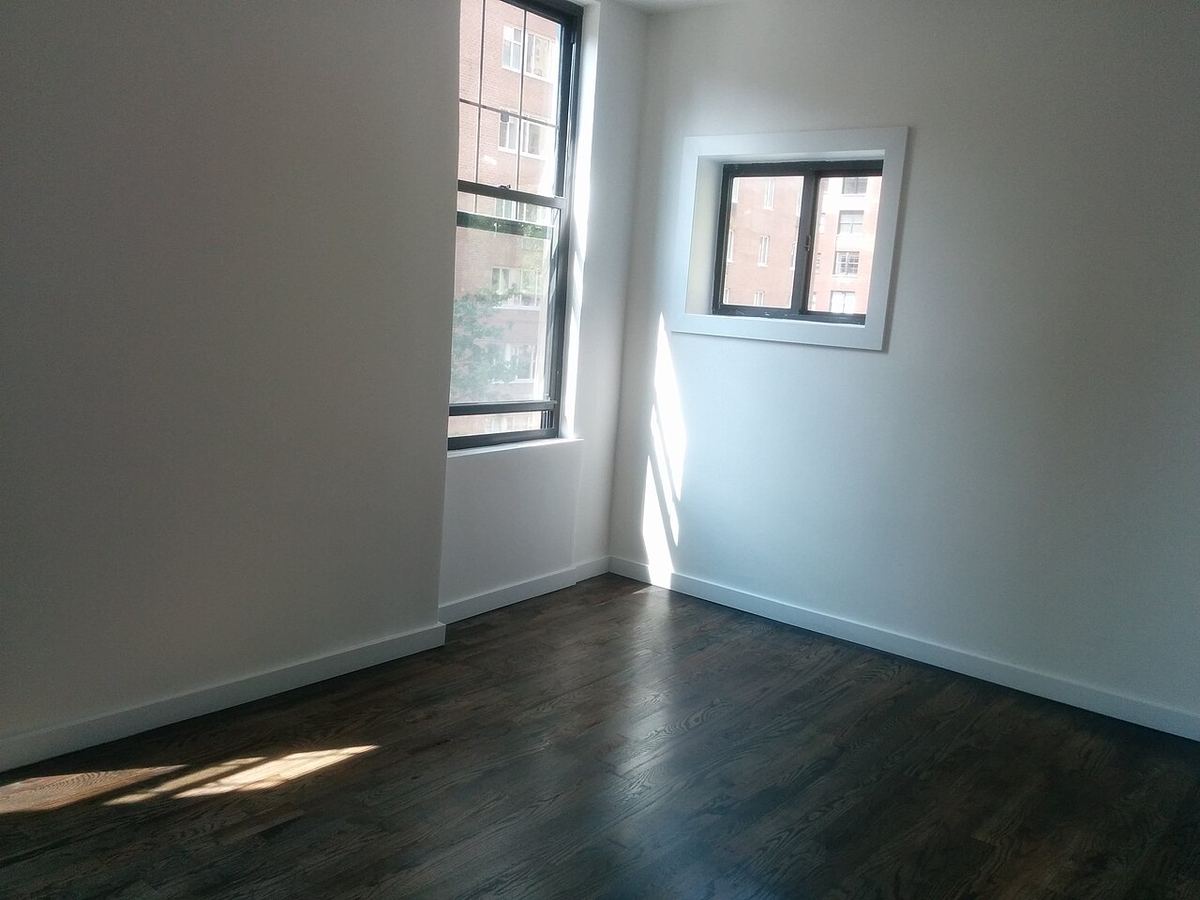 Lege kamer met een houten vloer en daglicht door twee ramen