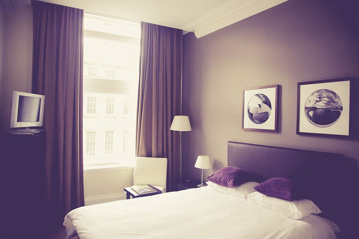 Slaapkamer met een opgemaakt bed, een leeslamp en lange gordijnen