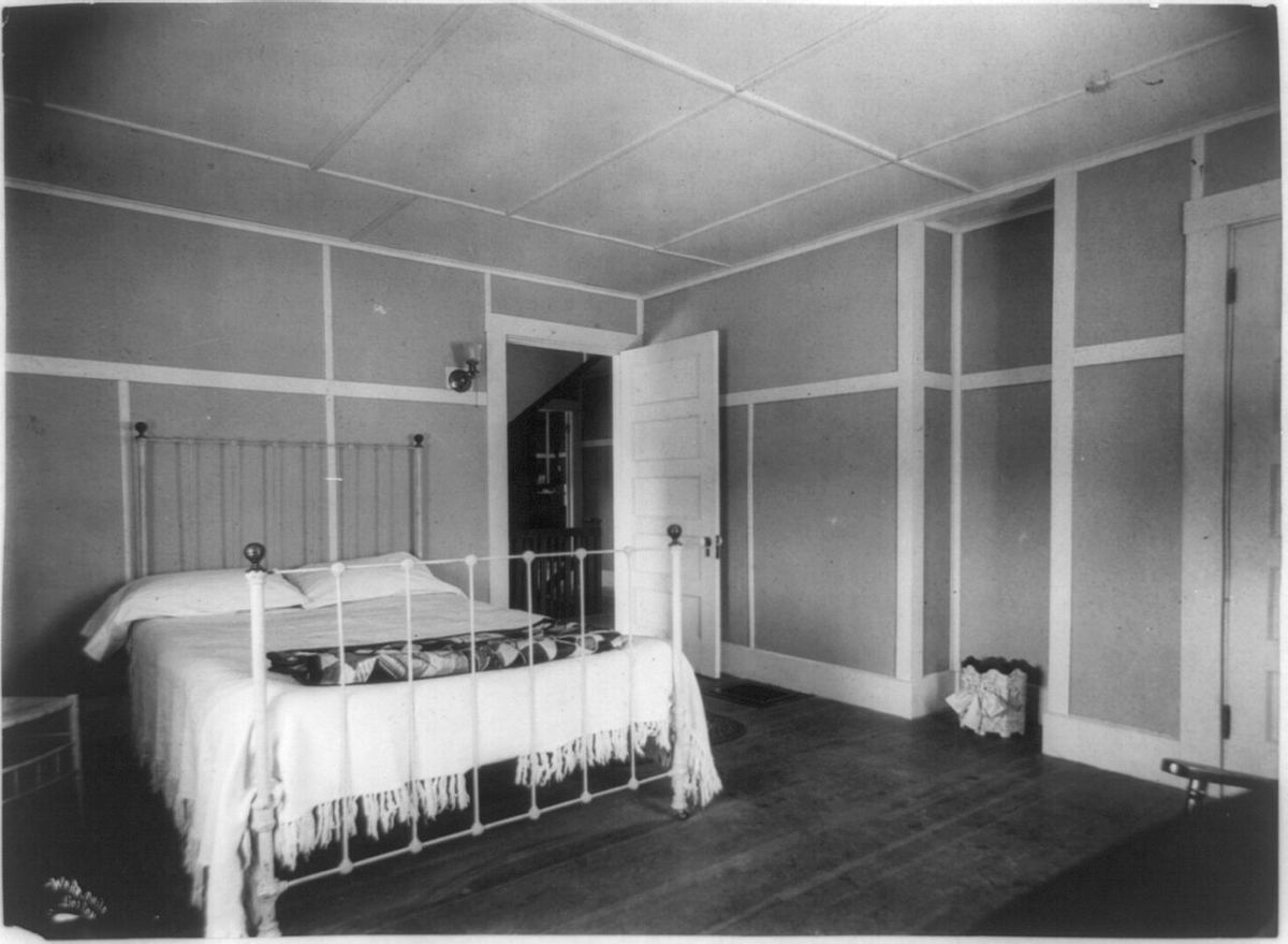 Zwart-witfoto van een sobere slaapkamer met een ijzeren bed