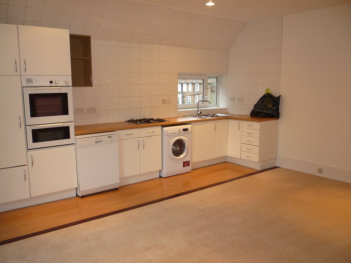 Kleine witte keuken met een houten vloer en bijna lege werkbladen