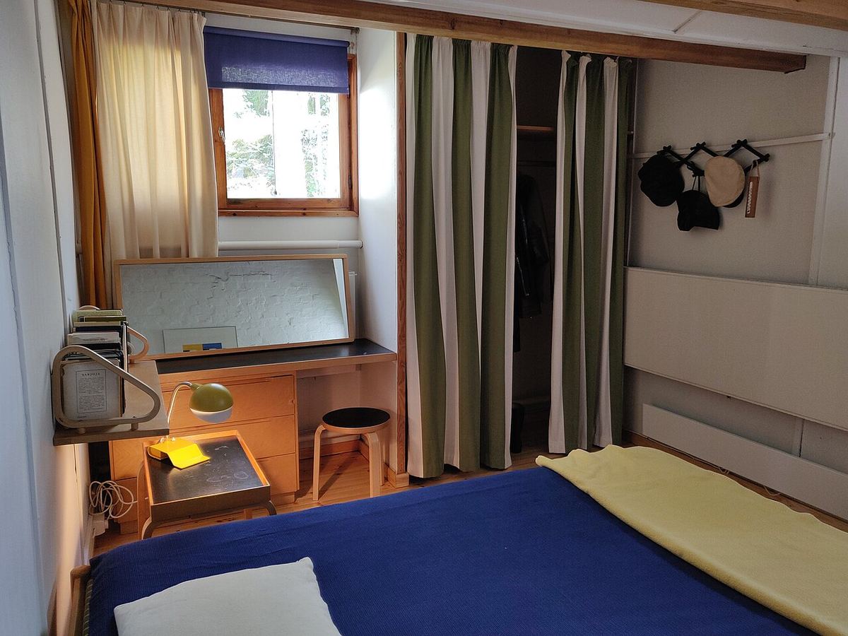 Compact interieur met een bed, een kleine werkplek en hoge ramen