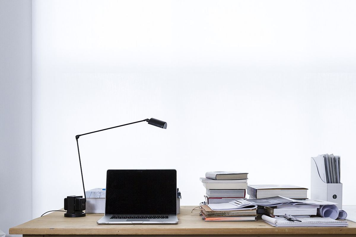 Opgeruimd bureau met een laptop, een lamp en een stapel boeken