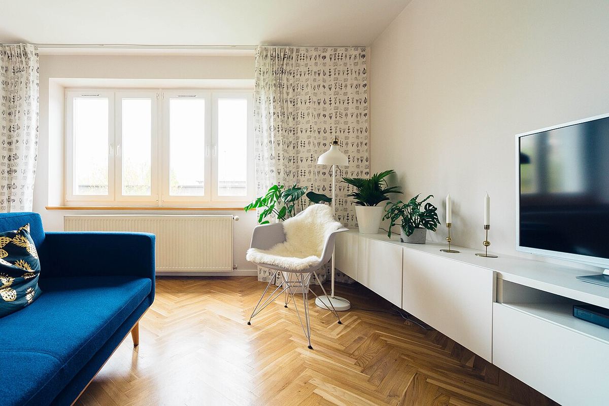 Lichte woonkamer met een blauwe bank, een wit tv-meubel en planten